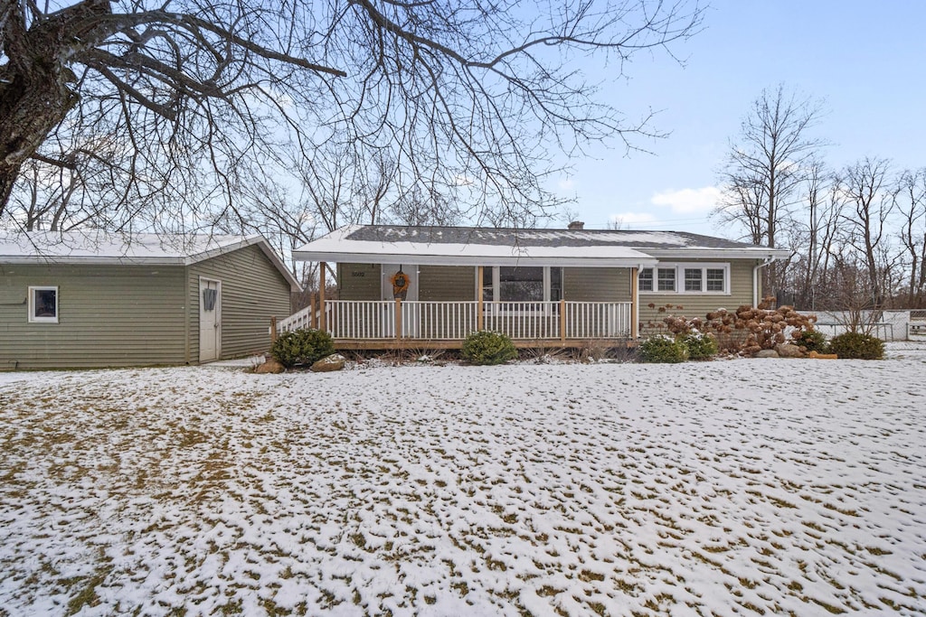 snow covered rear of property featuring covered porch