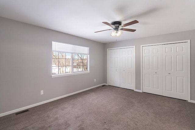 unfurnished bedroom featuring baseboards, carpet, visible vents, and two closets