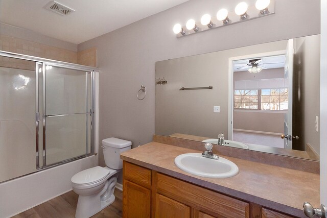 full bathroom featuring ceiling fan, hardwood / wood-style floors, bath / shower combo with glass door, vanity, and toilet