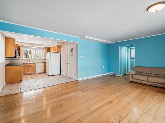 unfurnished living room with a sink, visible vents, baseboards, light wood finished floors, and crown molding