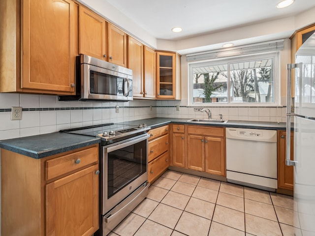 kitchen featuring a sink, appliances with stainless steel finishes, backsplash, dark countertops, and glass insert cabinets