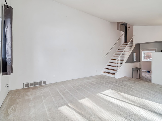 unfurnished living room featuring lofted ceiling, stairway, visible vents, and light colored carpet