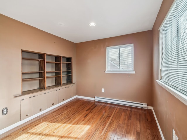 spare room featuring a baseboard heating unit, recessed lighting, wood-type flooring, and baseboards