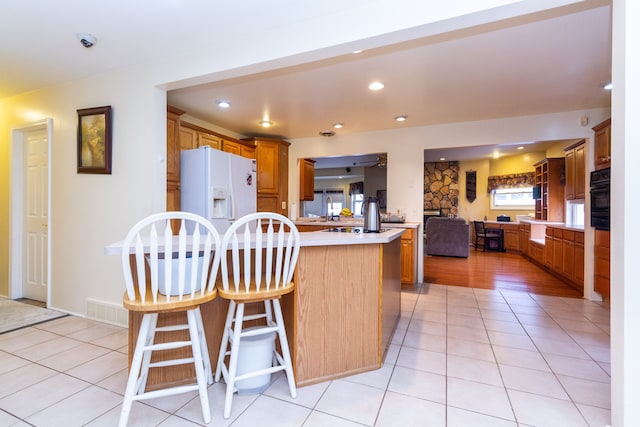 kitchen featuring white fridge with ice dispenser, light tile patterned floors, black oven, kitchen peninsula, and a breakfast bar area