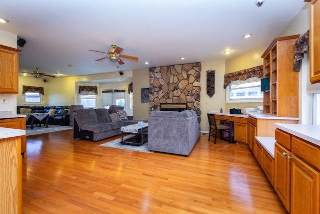 living room featuring a stone fireplace, ceiling fan, and light hardwood / wood-style floors