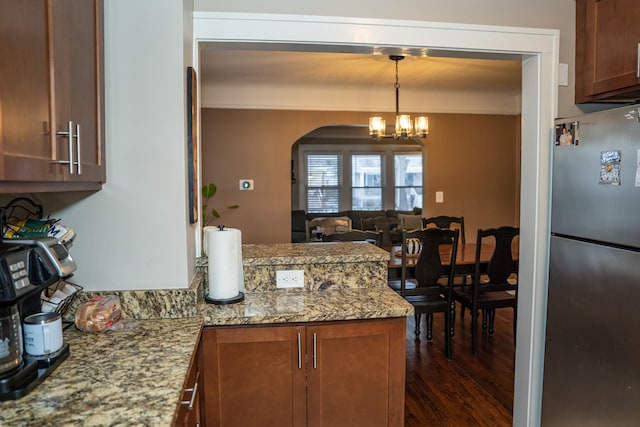 kitchen featuring light stone countertops, dark wood-type flooring, pendant lighting, a notable chandelier, and stainless steel refrigerator