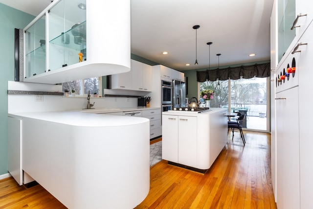 kitchen featuring a center island, sink, light hardwood / wood-style flooring, decorative light fixtures, and white cabinetry