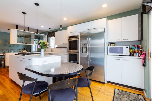 kitchen featuring stainless steel appliances, sink, light hardwood / wood-style floors, white cabinetry, and hanging light fixtures