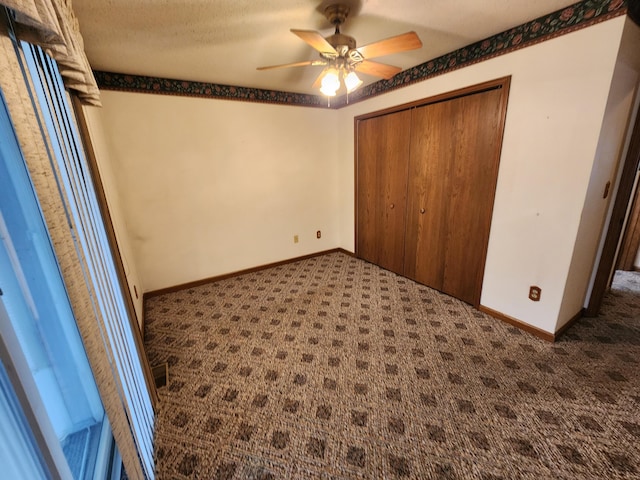 unfurnished bedroom with dark colored carpet, a textured ceiling, a closet, and ceiling fan