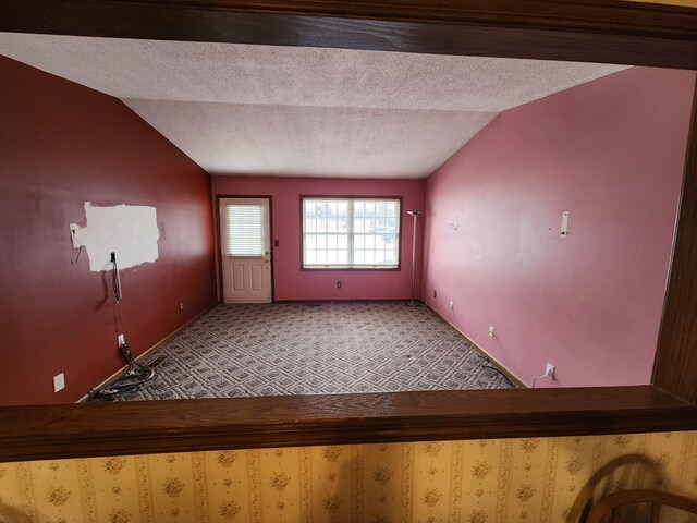 carpeted foyer entrance featuring a textured ceiling and vaulted ceiling
