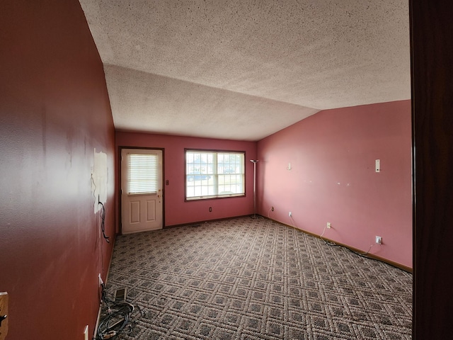 empty room featuring a textured ceiling, dark carpet, and lofted ceiling