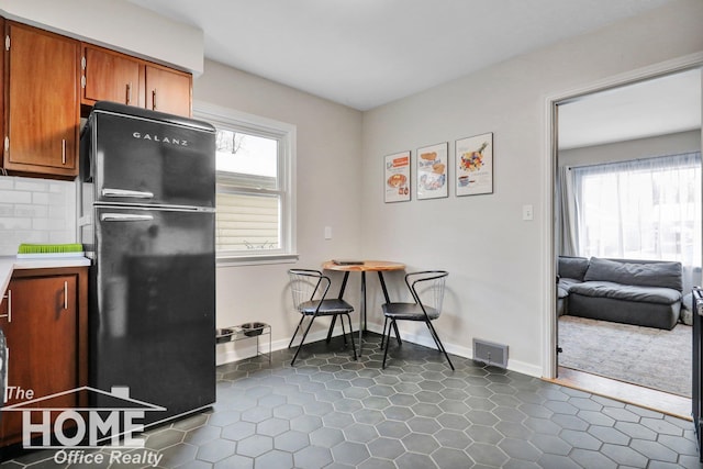 kitchen featuring dark tile patterned flooring, black refrigerator, a wealth of natural light, and tasteful backsplash