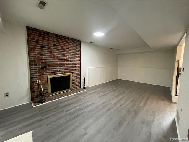 unfurnished living room with wood-type flooring and a brick fireplace