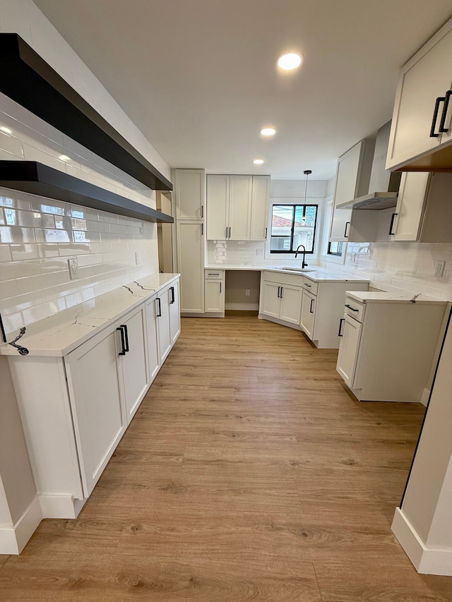 kitchen featuring white cabinets, light wood-style floors, decorative light fixtures, wall chimney range hood, and backsplash