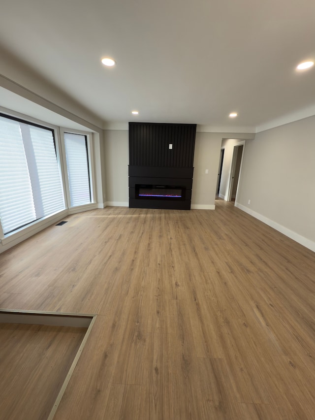 unfurnished living room with recessed lighting, a fireplace, baseboards, and wood finished floors