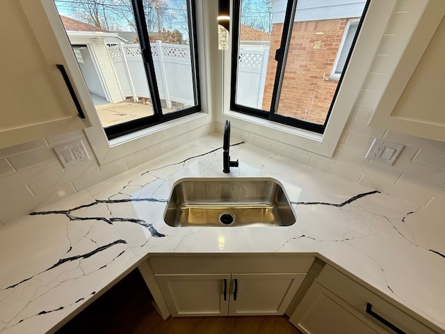 interior details with tasteful backsplash, white cabinets, a sink, and light stone countertops