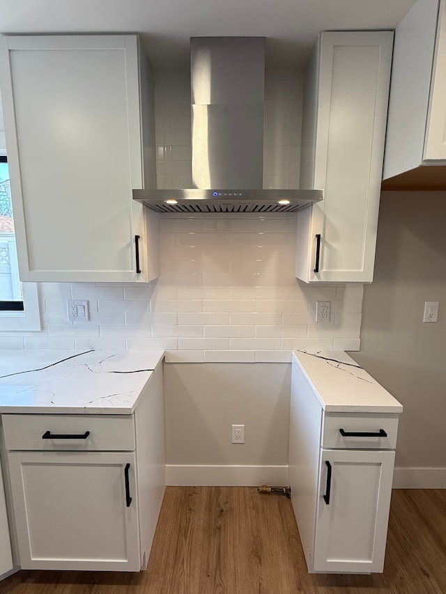 kitchen featuring wall chimney range hood, light wood-style flooring, white cabinetry, and light stone countertops