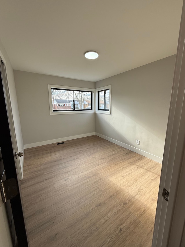 unfurnished room featuring light wood finished floors, visible vents, and baseboards