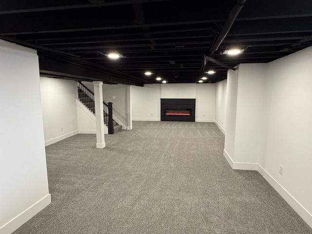 finished below grade area featuring a lit fireplace, stairway, carpet flooring, and baseboards