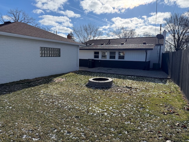 back of property with brick siding, a lawn, central AC unit, a fenced backyard, and a fire pit