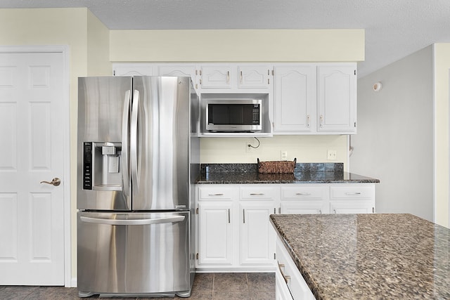 kitchen with a textured ceiling, stainless steel appliances, dark tile patterned flooring, dark stone countertops, and white cabinets