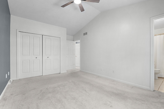 unfurnished bedroom with ensuite bath, light colored carpet, vaulted ceiling, ceiling fan, and a closet