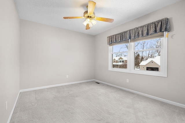 spare room with a textured ceiling, light colored carpet, and ceiling fan