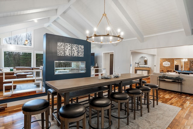 dining space with beam ceiling, high vaulted ceiling, light wood-type flooring, and an inviting chandelier