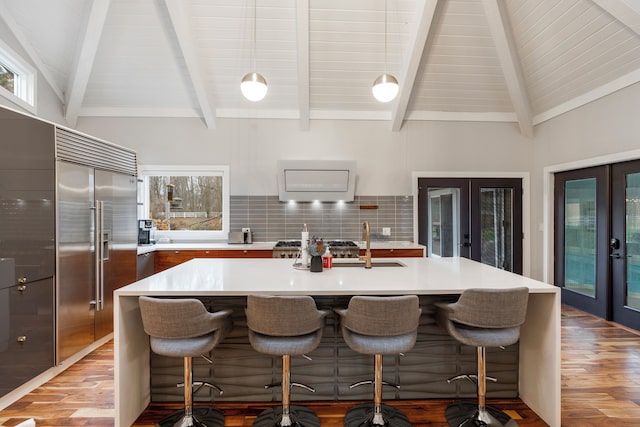 kitchen with a kitchen island with sink, lofted ceiling with beams, french doors, and stainless steel built in refrigerator