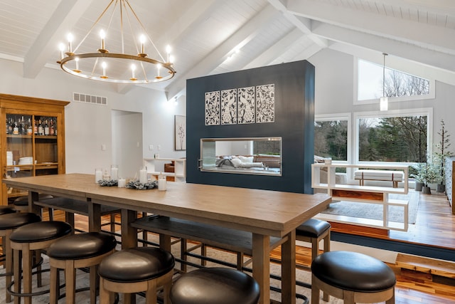 dining space with beamed ceiling, high vaulted ceiling, wooden ceiling, a notable chandelier, and hardwood / wood-style flooring