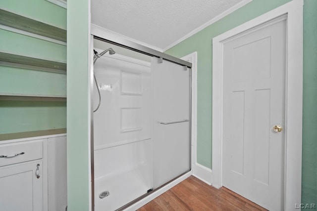 bathroom featuring a shower with door, wood-type flooring, a textured ceiling, and ornamental molding