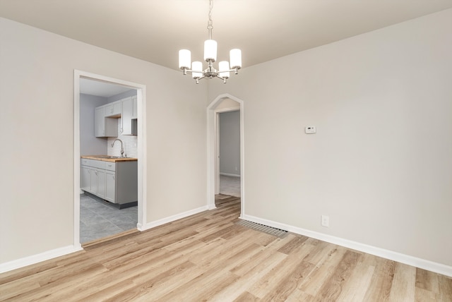 spare room featuring sink, a chandelier, and light hardwood / wood-style flooring