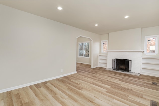 unfurnished living room with light wood-type flooring, a fireplace, and a wealth of natural light