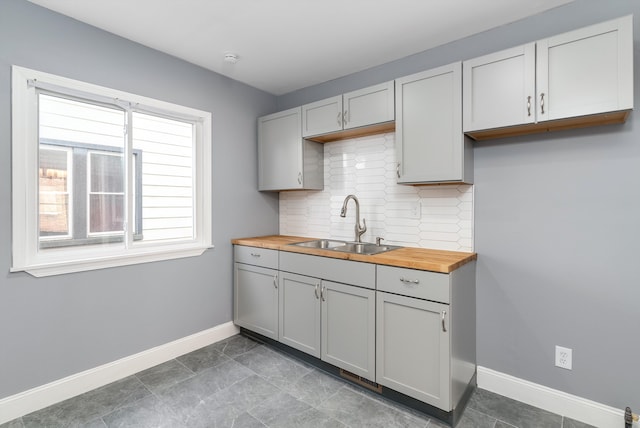 kitchen with backsplash, gray cabinetry, sink, and wood counters