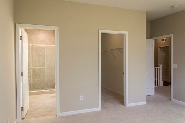 unfurnished bedroom featuring connected bathroom, light colored carpet, a spacious closet, and a closet