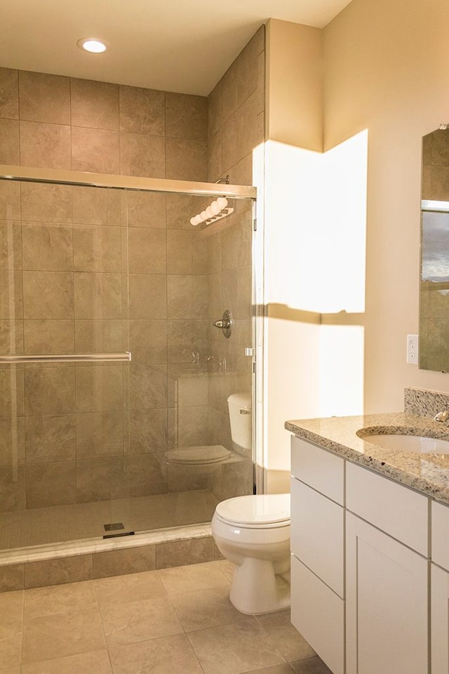 bathroom featuring tile patterned flooring, vanity, a shower with shower door, and toilet