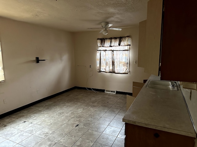 unfurnished dining area with ceiling fan, sink, and a textured ceiling