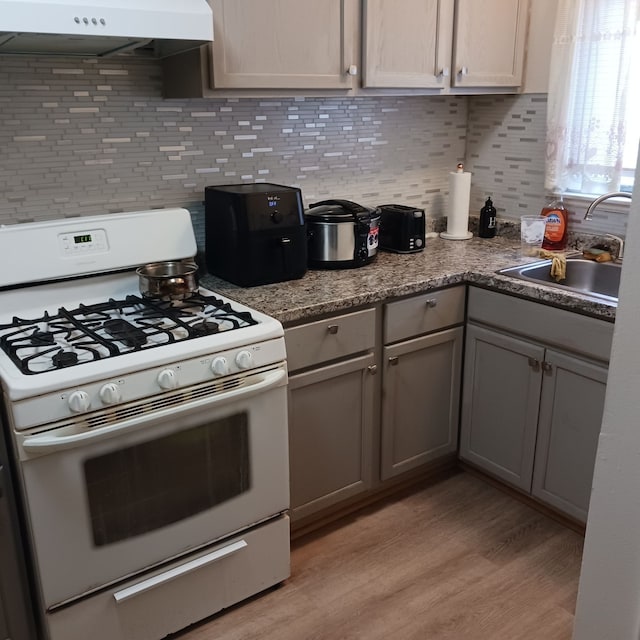 kitchen featuring backsplash, white gas range oven, extractor fan, sink, and gray cabinets