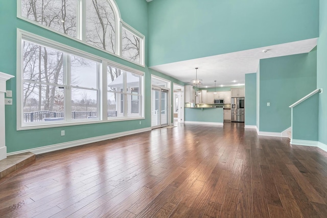 unfurnished living room with a tiled fireplace, dark hardwood / wood-style flooring, a chandelier, and a high ceiling