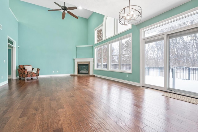 unfurnished living room featuring a tiled fireplace, hardwood / wood-style floors, a towering ceiling, and ceiling fan with notable chandelier