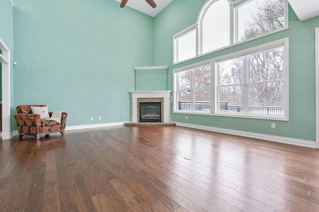 unfurnished living room with a wealth of natural light, ceiling fan, a high ceiling, wood-type flooring, and a fireplace