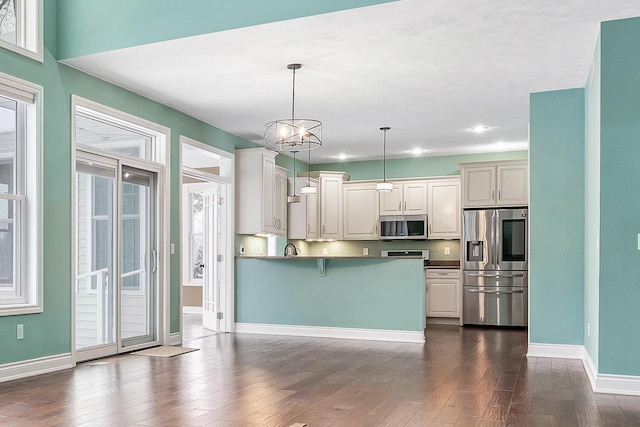 kitchen with dark wood-type flooring, a notable chandelier, kitchen peninsula, decorative light fixtures, and appliances with stainless steel finishes