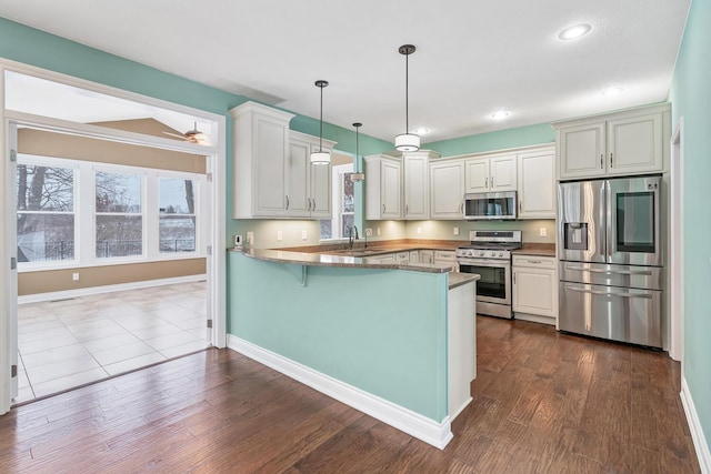 kitchen with sink, kitchen peninsula, pendant lighting, white cabinets, and appliances with stainless steel finishes