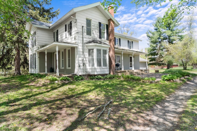 rear view of house with a chimney, a porch, a patio area, and a lawn
