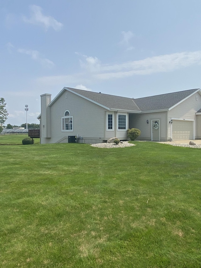 rear view of property featuring central AC, a garage, and a lawn