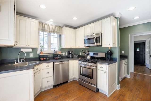 kitchen with white cabinets, sink, ornamental molding, appliances with stainless steel finishes, and dark hardwood / wood-style flooring