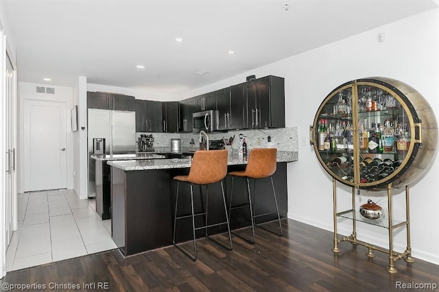 kitchen with decorative backsplash, kitchen peninsula, light stone counters, stainless steel appliances, and light tile patterned floors