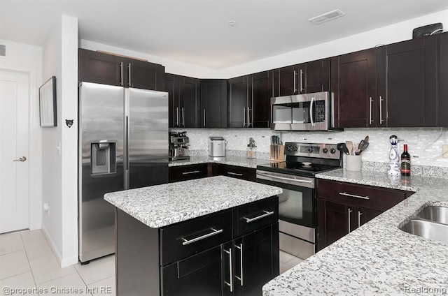 kitchen featuring decorative backsplash, appliances with stainless steel finishes, dark brown cabinetry, a center island, and light tile patterned flooring