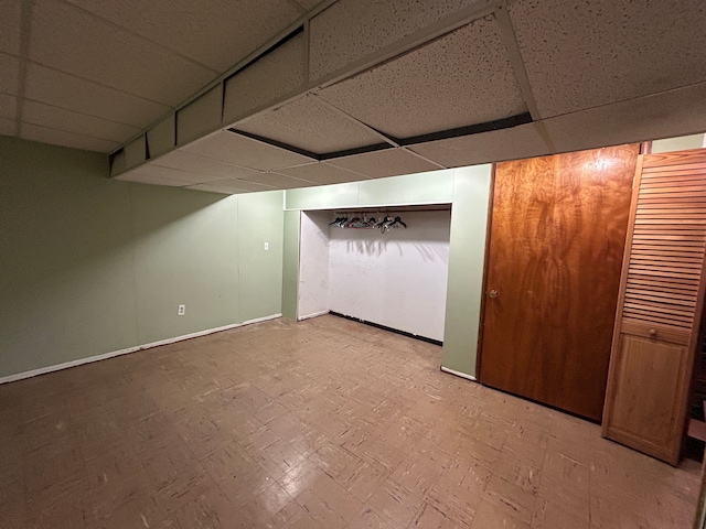 finished basement with light floors, a drop ceiling, and baseboards