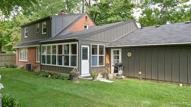 back of property with cooling unit, a sunroom, and a lawn